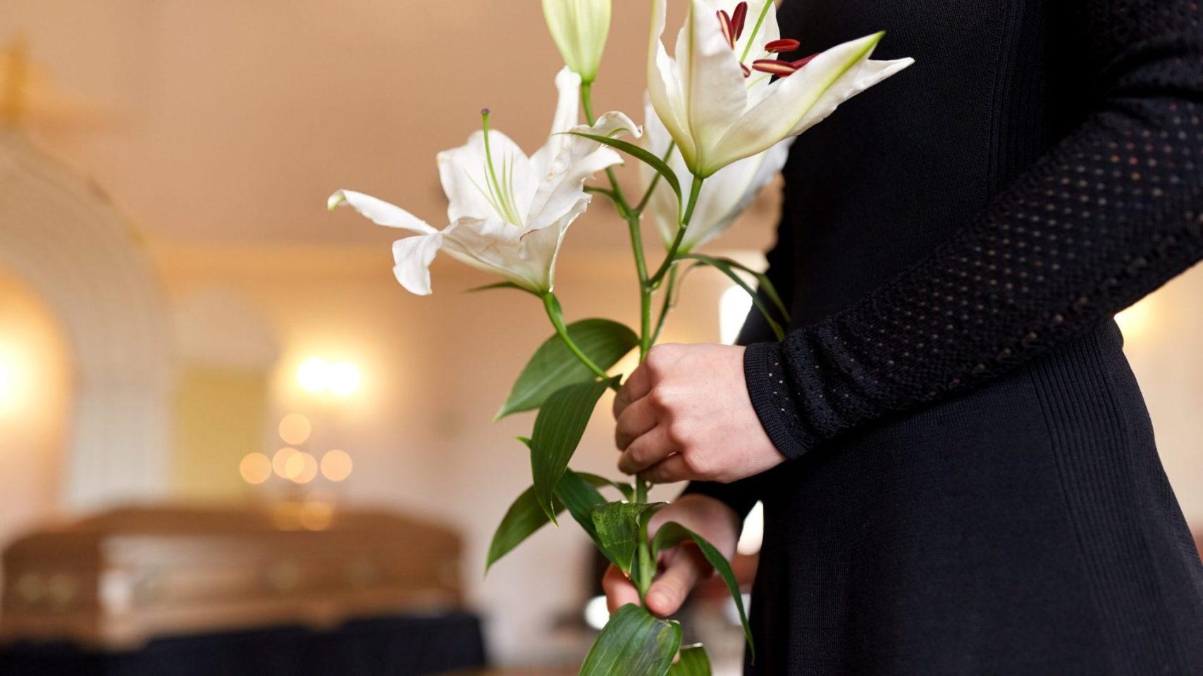 Person holding a white lily during a traditional funeral service