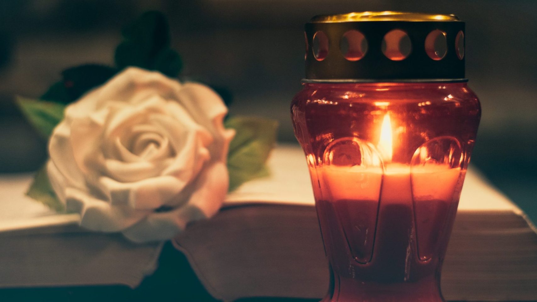 Candle and white rose placed beside a book for a memorial service