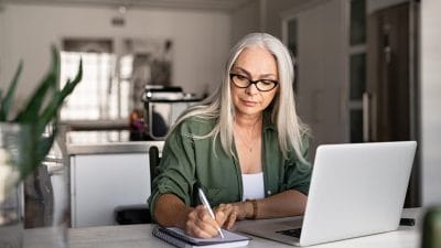 Woman comparing Houston cremation costs online while taking notes at home