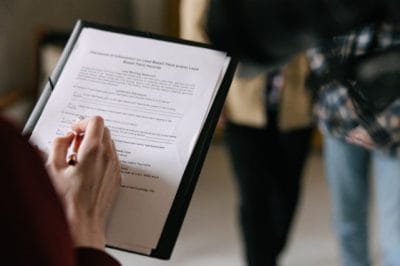 A person fills out paperwork on a clipboard while others stand nearby, suggesting a formal or administrative process.