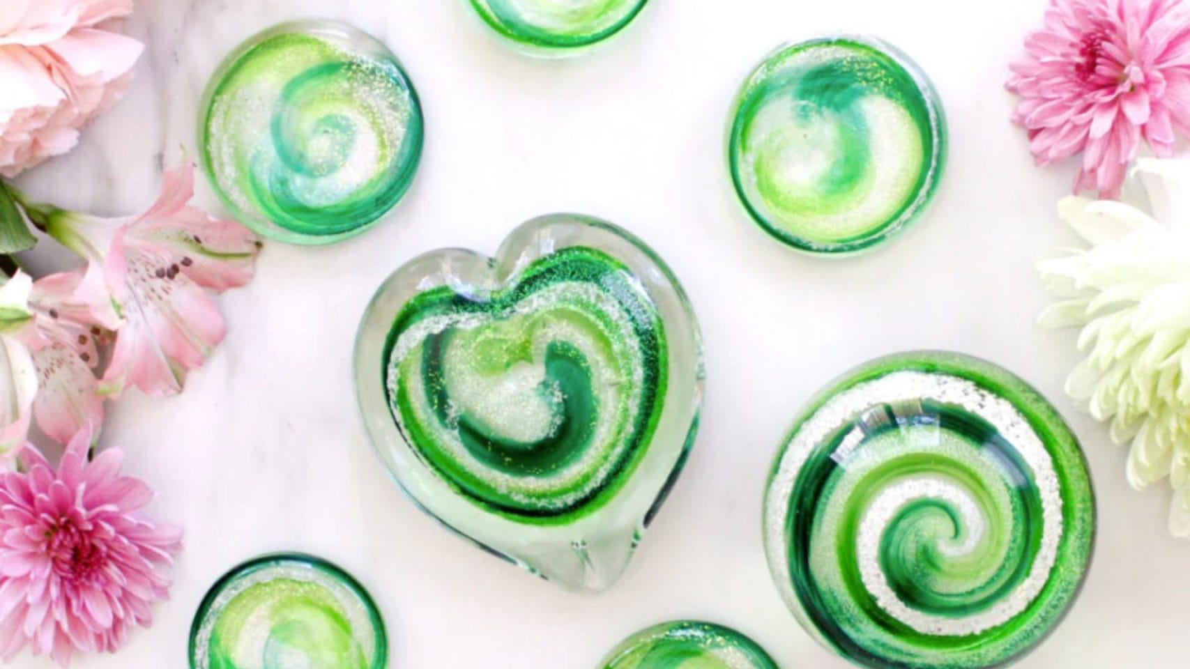 Green cremation glass heart, touchstones, and orb surrounded by flowers