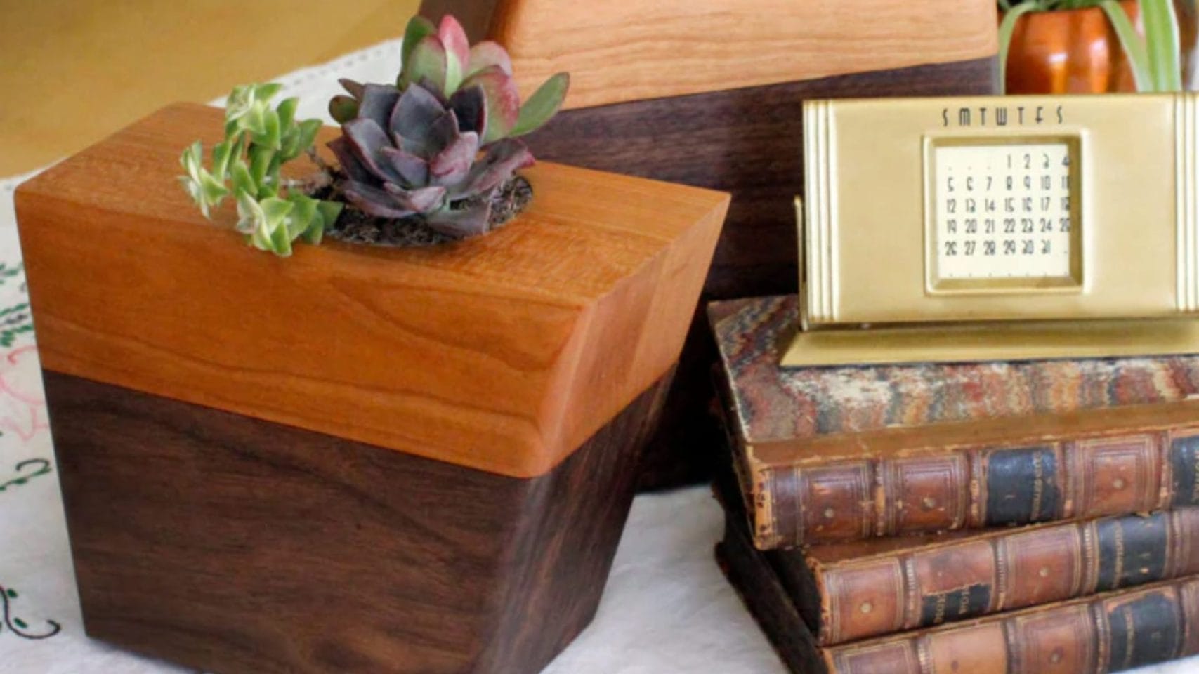 Decorative wooden memorial urn displayed on a table with books and plants.
