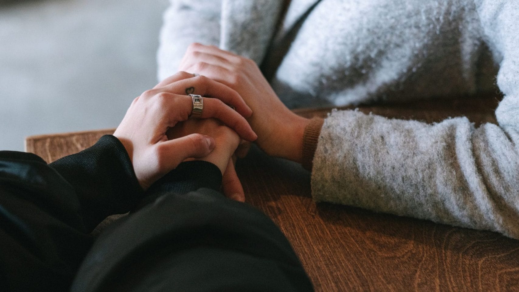 Two people holding hands at a table during a difficult family conversation.