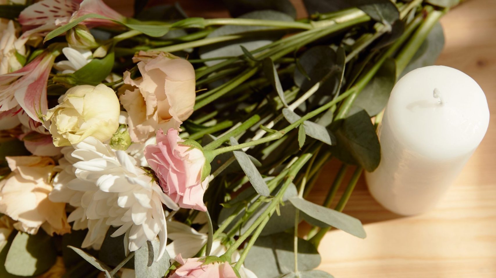Flowers and a white candle arranged for a memorial gathering