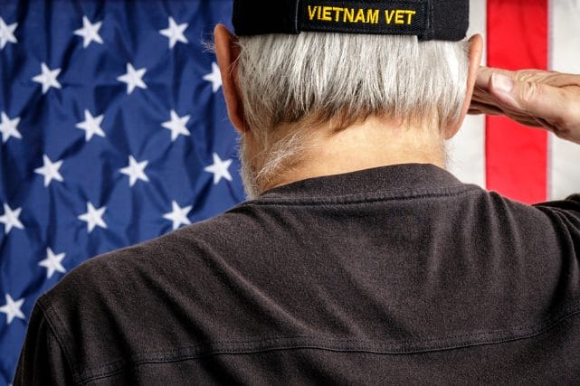 Vietnam veteran saluting near American flag for veteran cremation discounts and military honors