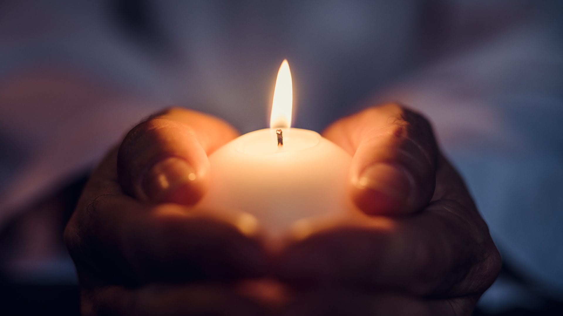 Hands holding a lit memorial candle representing affordable cremation services in Houston