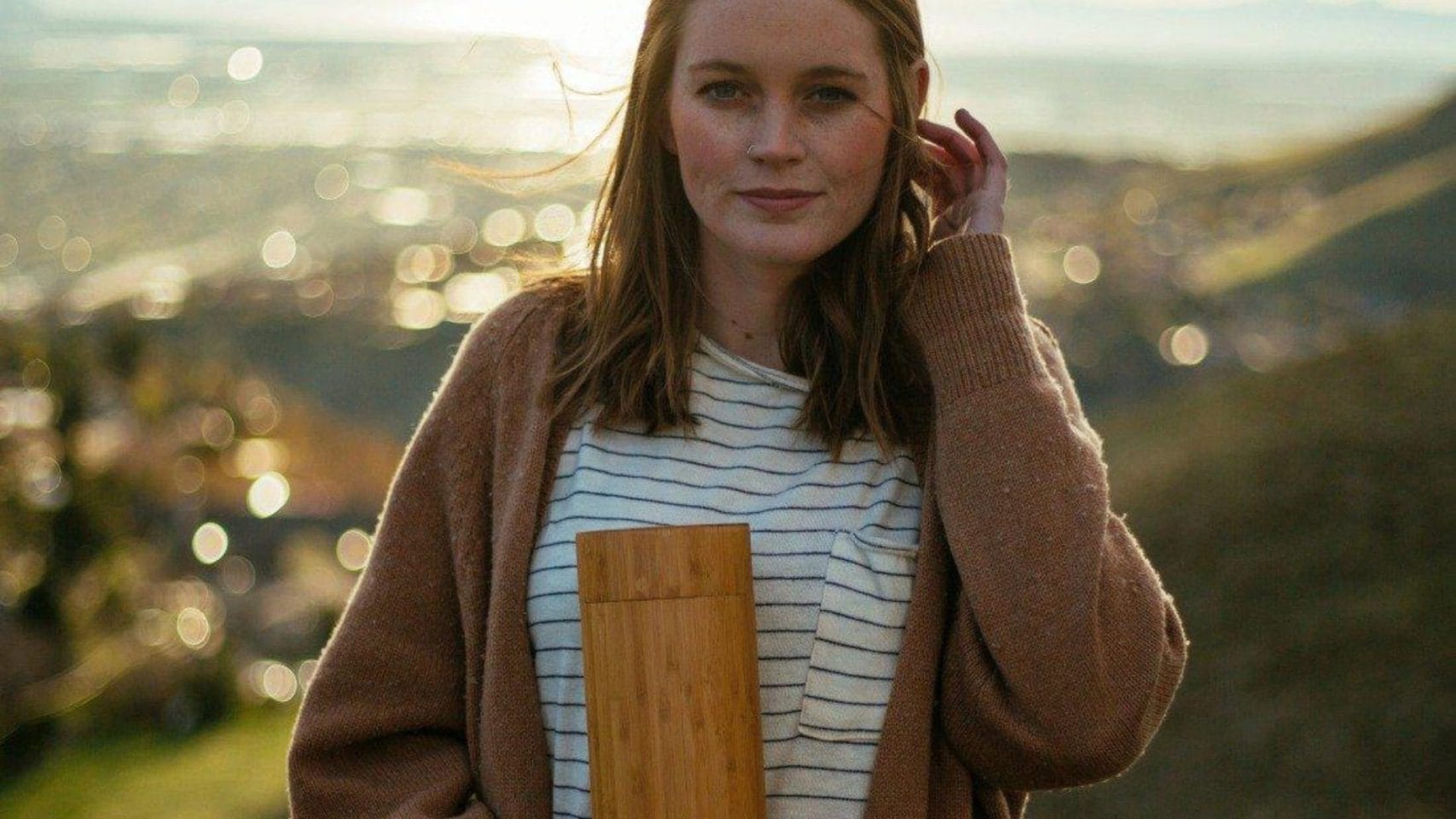 Person holding a wooden scattering urn outdoors in a peaceful setting.