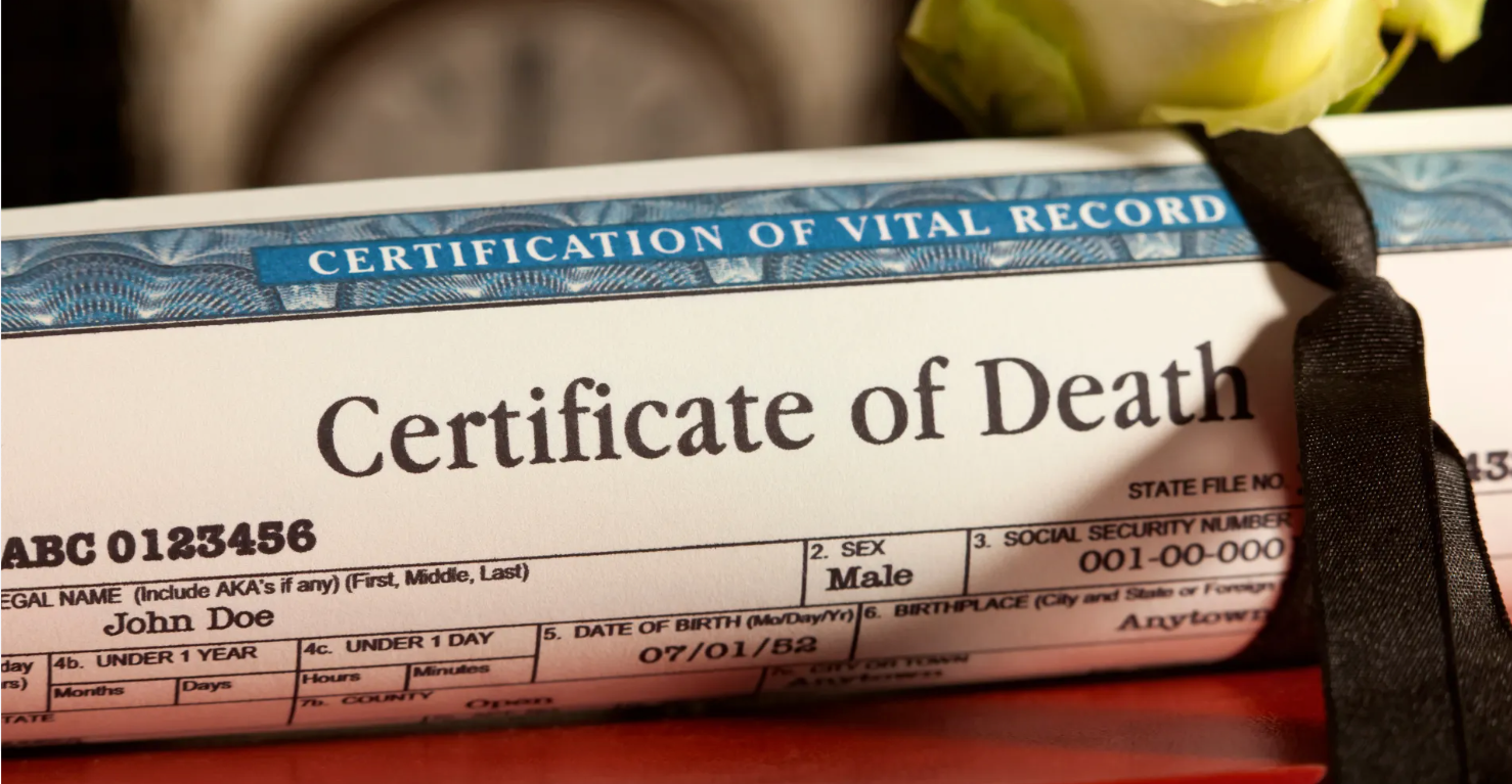 Close-up of a Certificate of Death with a black mourning ribbon and white rose resting on top.