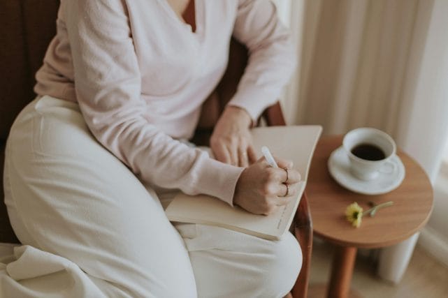 Person writing in a notebook near a window, representing thoughtful guidance when choosing a cremation provider in Houston.