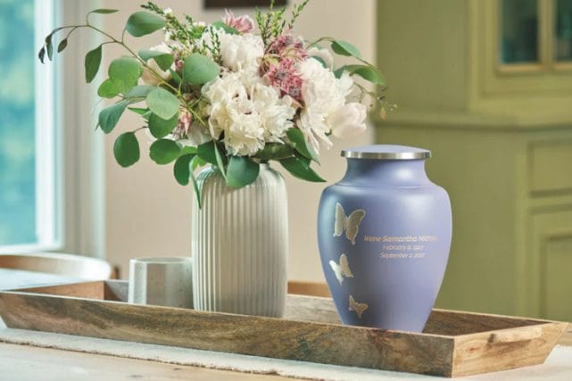 Decorative traditional cremation urn with butterfly design displayed beside a floral arrangement in a serene home setting.