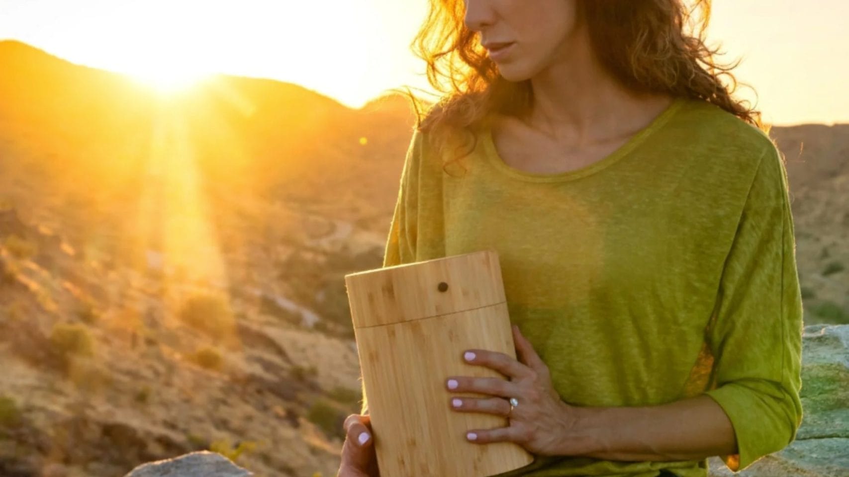 Woman holding a wooden urn outdoors at sunset, representing travel-friendly cremation urn options.