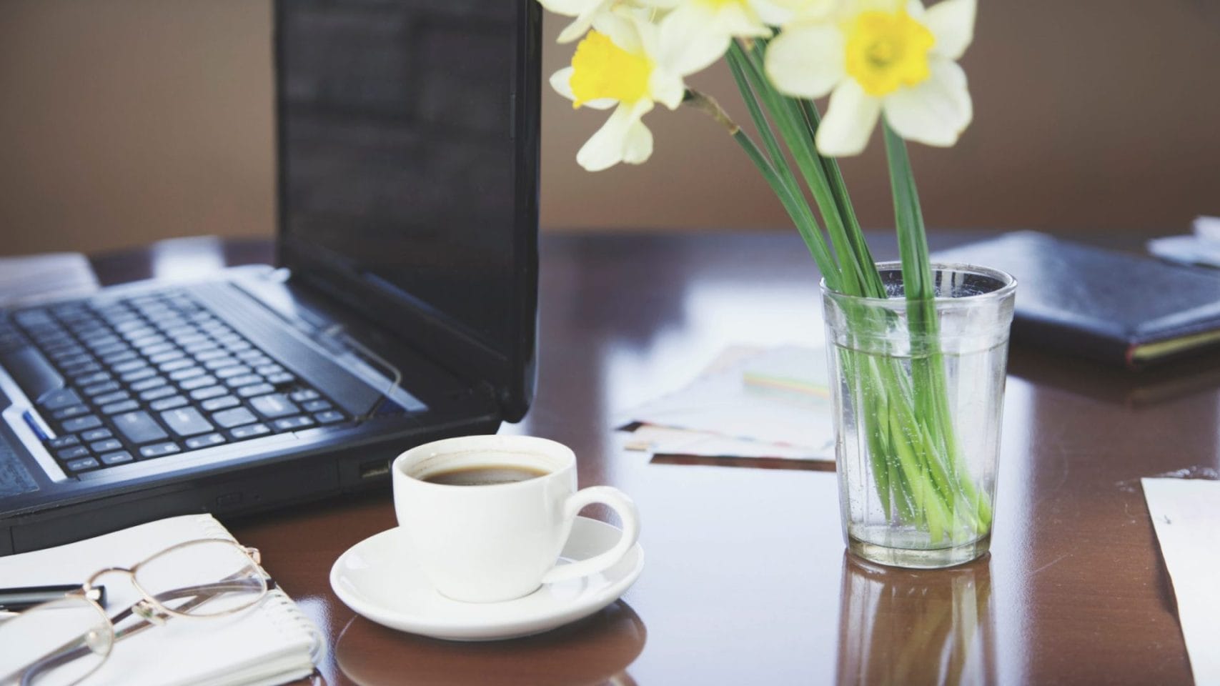 Desk with laptop, coffee, flowers, and paperwork