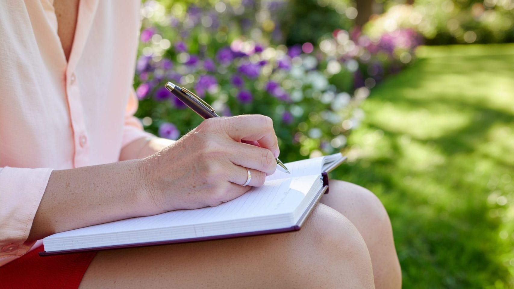 Person writing obituary notes in a notebook outdoors.